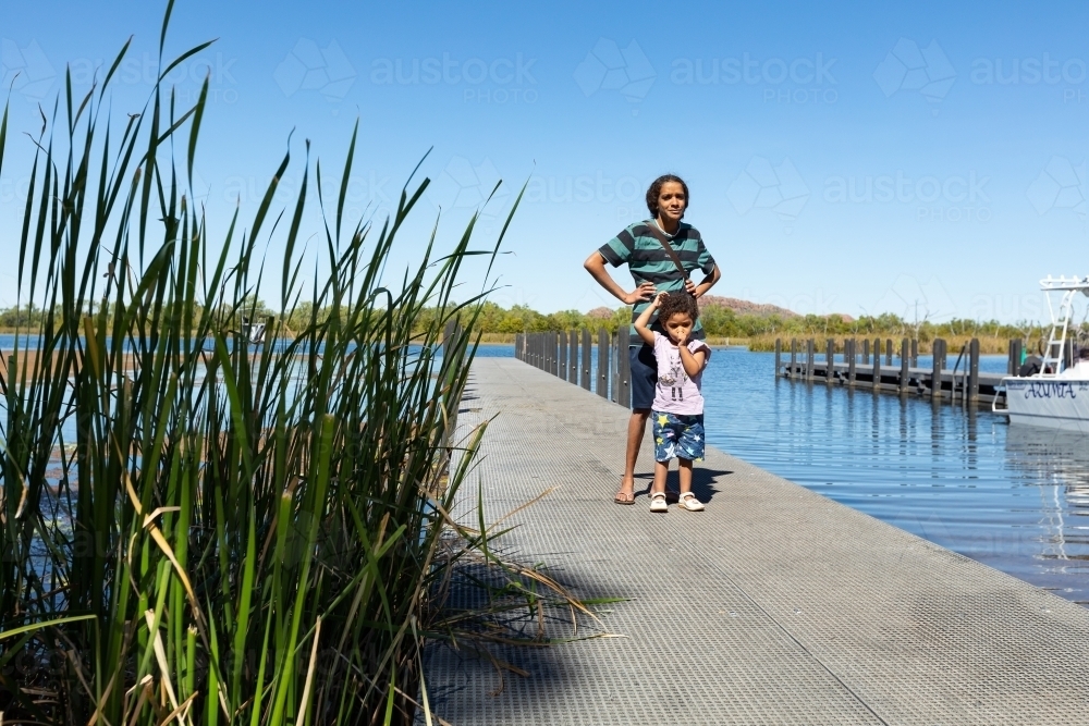 reeds in foreground with mother and child standing on jetty - Australian Stock Image