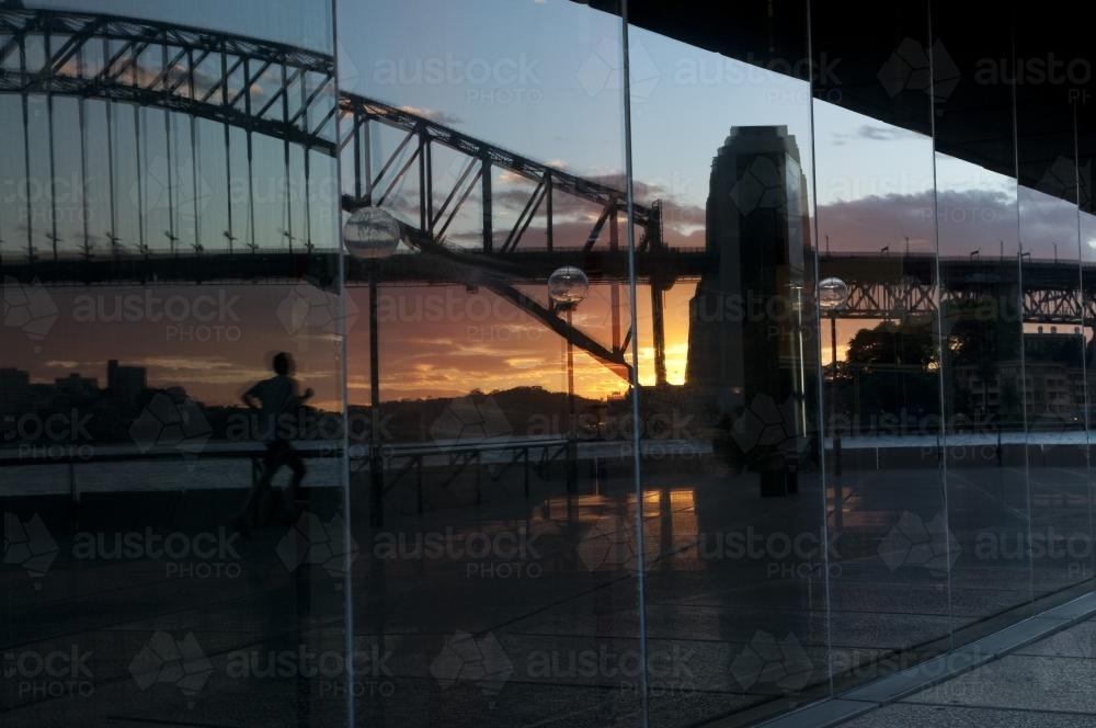 Reflection of a runner and the Harbour Bridge in Opera House windows - Australian Stock Image