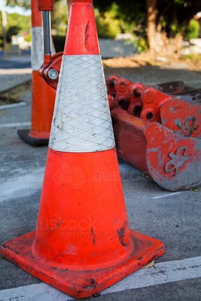 Reflective orange traffic cone beside excavator - Australian Stock Image