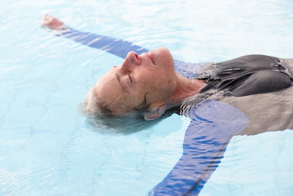 Relaxed active senior lady floating in swimming pool - Australian Stock Image