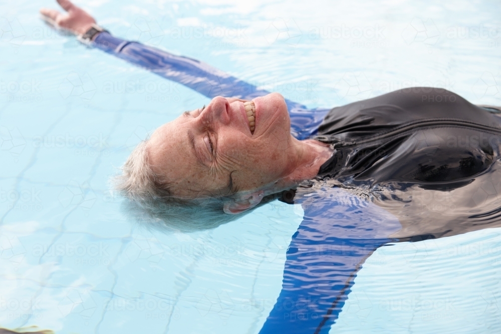 Relaxed active senior lady floating in swimming pool - Australian Stock Image