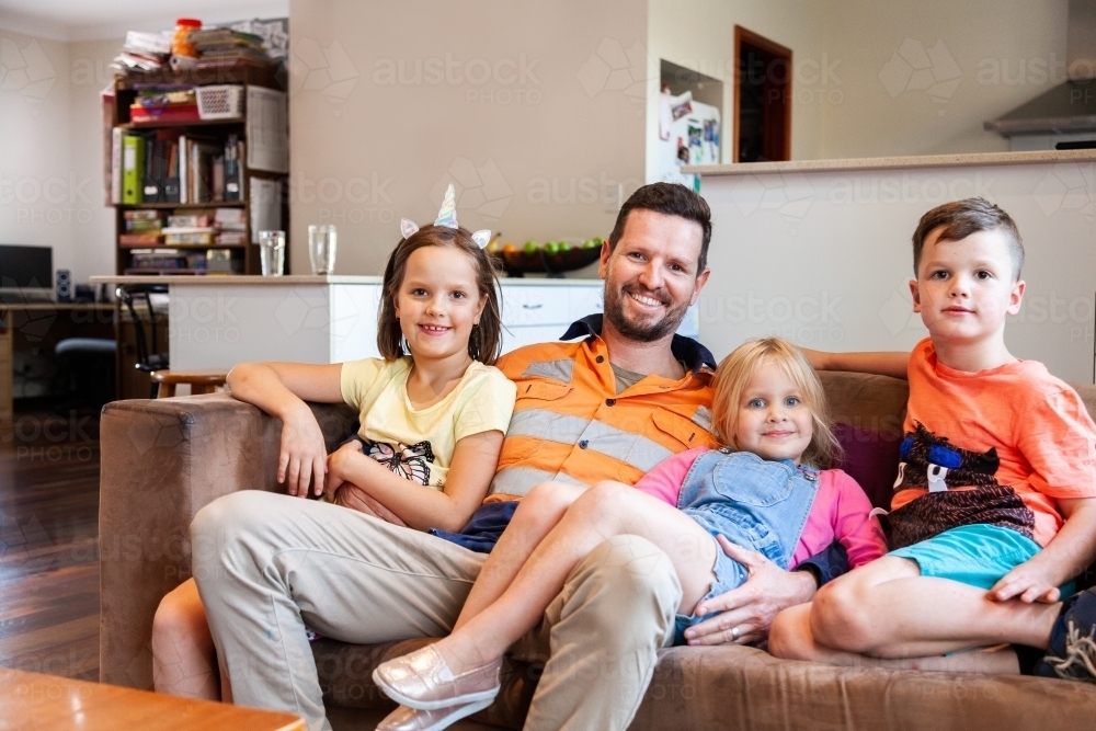 Relaxed tradie hanging out with his kids on lounge - Australian Stock Image