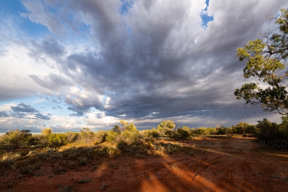 Remote Desert landscape with stormy cloud patterns and long shadows in the red sand. - Australian Stock Image