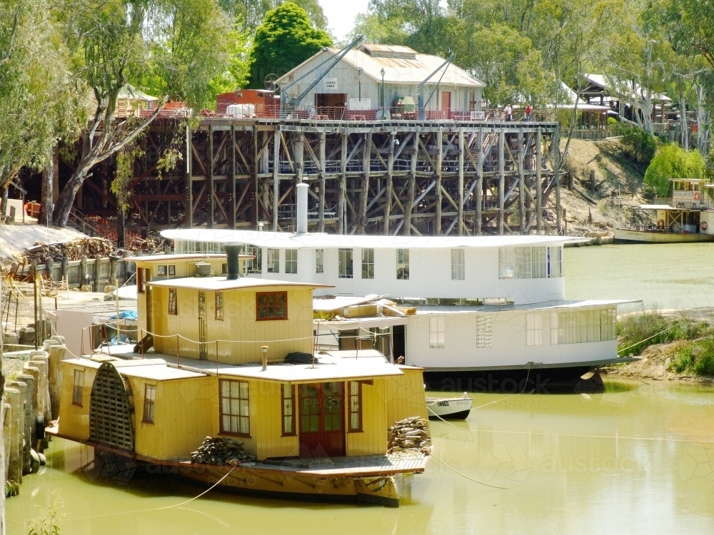 Restored paddle steamers sitting in a river below a wooden wharf - Australian Stock Image