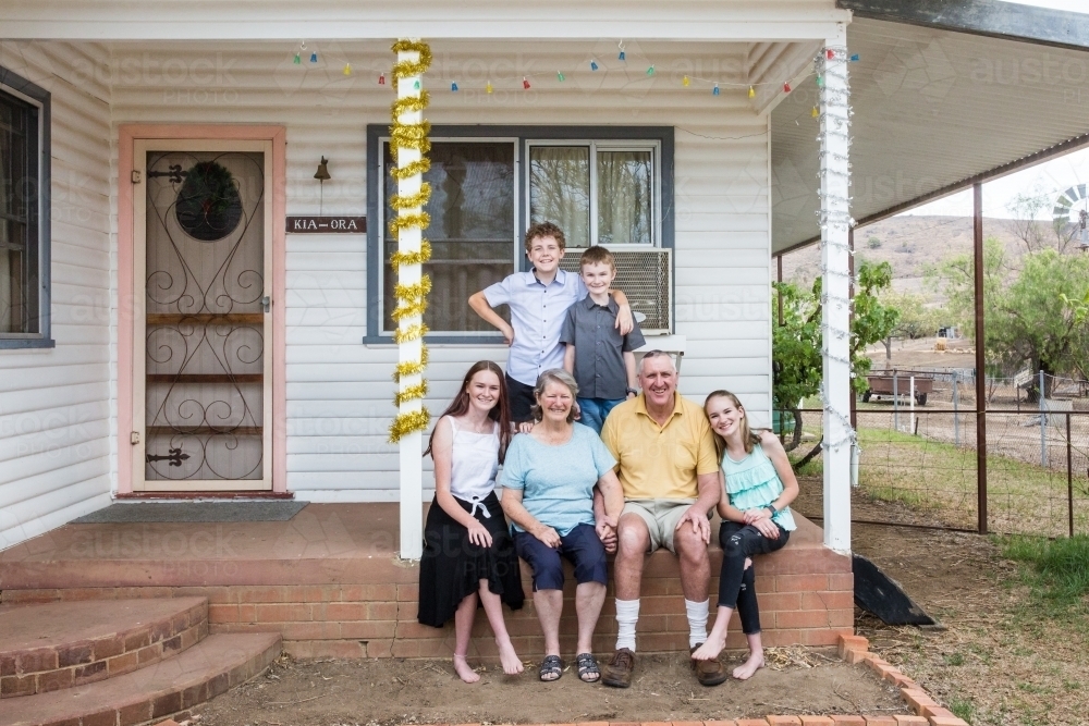 Retired grandparents sitting on front verandah of house with grandchildren happy - Australian Stock Image