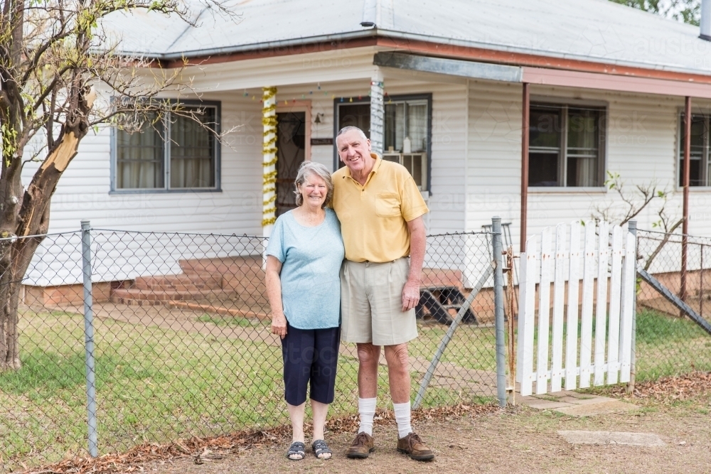 Retired older couple husband and wife standing together in front of house happy smiling - Australian Stock Image