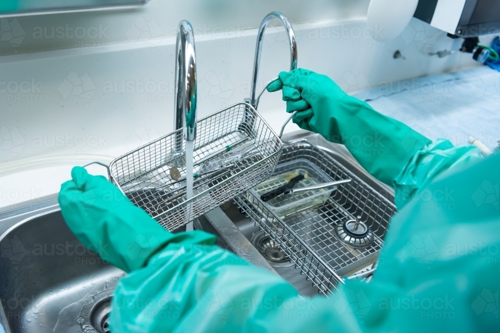 Rinsing and cleaning dental instruments under running water - Australian Stock Image