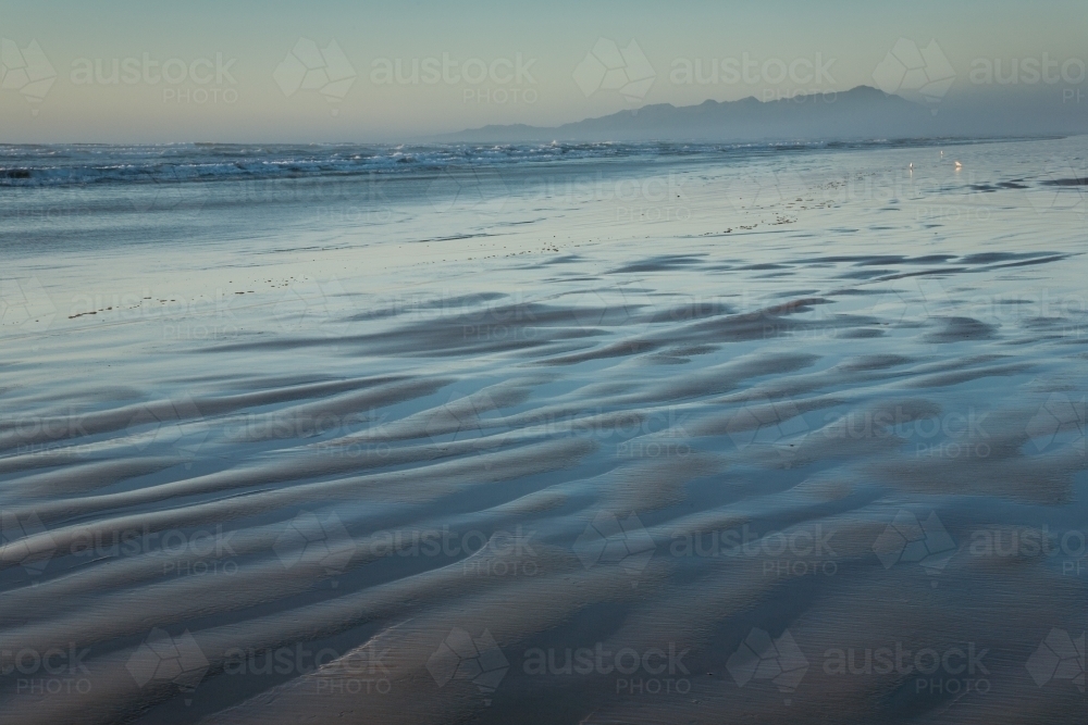 Ripples and blue water on beach with sea mist and distant mountains - Australian Stock Image