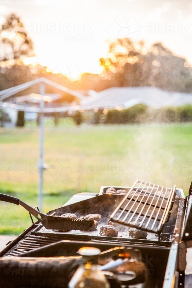 Rissoles cooking on a BBQ in the backyard at sunset - Australian Stock Image