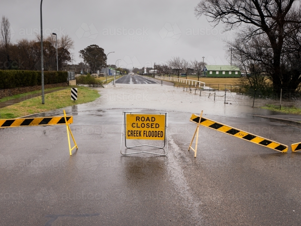 "ROAD CLOSED CREEK FLOODED" sign on underwater bitumen road - Australian Stock Image