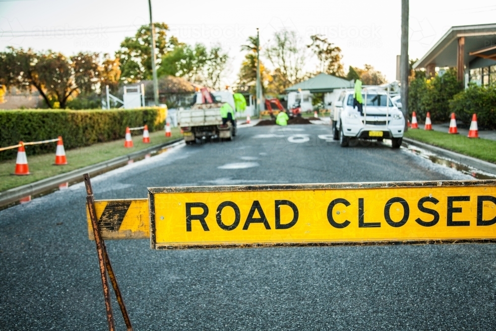 Road closed sign and water running over road from leaking water main - Australian Stock Image