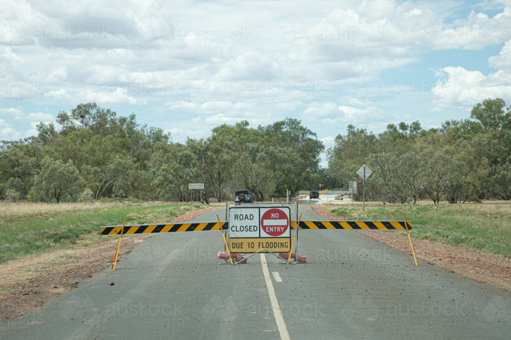 Road closed sign with vehicle driving through water behind - Australian Stock Image