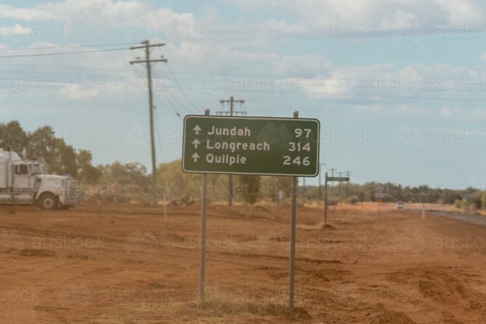 Road sign on dusty, red roadside with parked truck in background. - Australian Stock Image