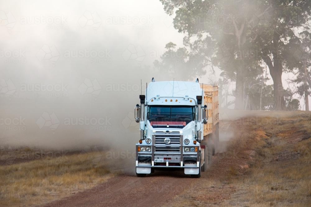 Road train truck driving down unsealed road creating dust - Australian Stock Image