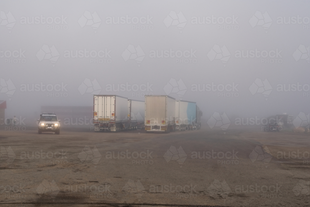 Road Trains parked at roadhouse shrouded in fog, Eyre Highway, South Australia - Australian Stock Image