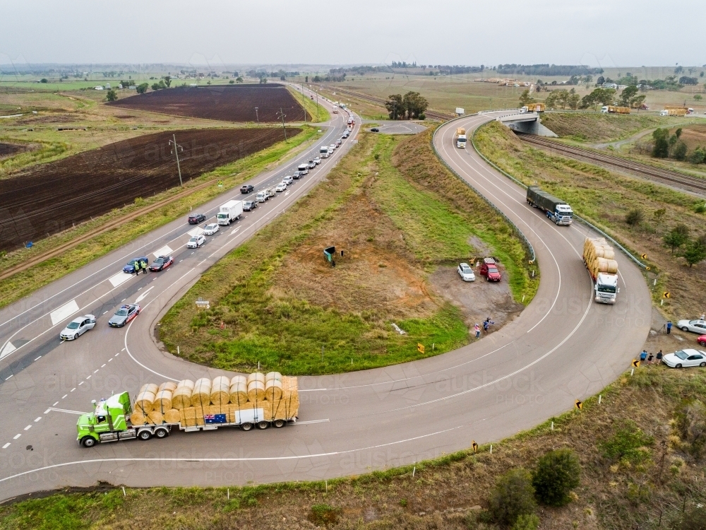 Road trains pulling out onto highway to continue journey delivering hay for drought relief - Australian Stock Image