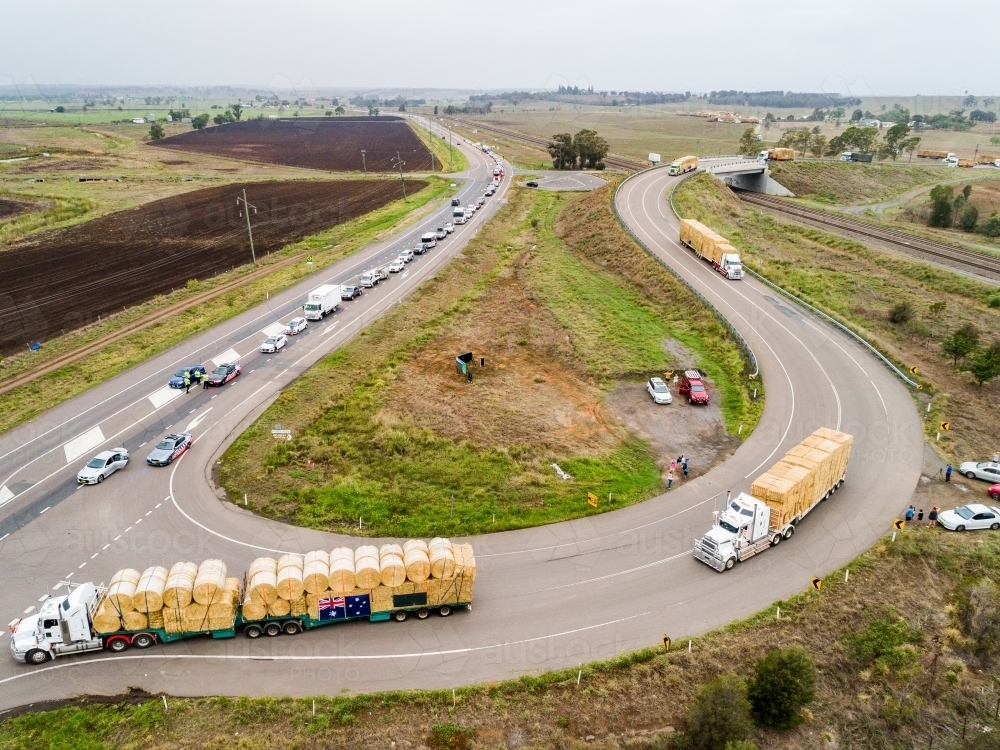 Road trains pulling out onto highway to continue journey delivering hay for drought relief - Australian Stock Image