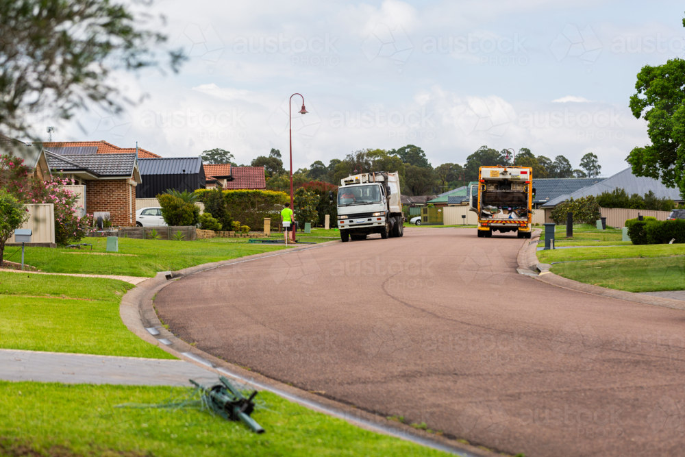 roadside pickup garbage removal trucks driving down street in town - Australian Stock Image
