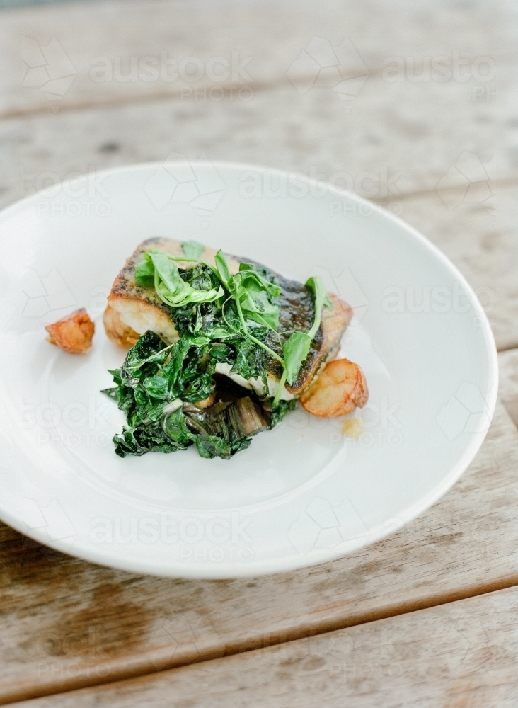 Roast potatoes, greens and fish on a white plate - Australian Stock Image