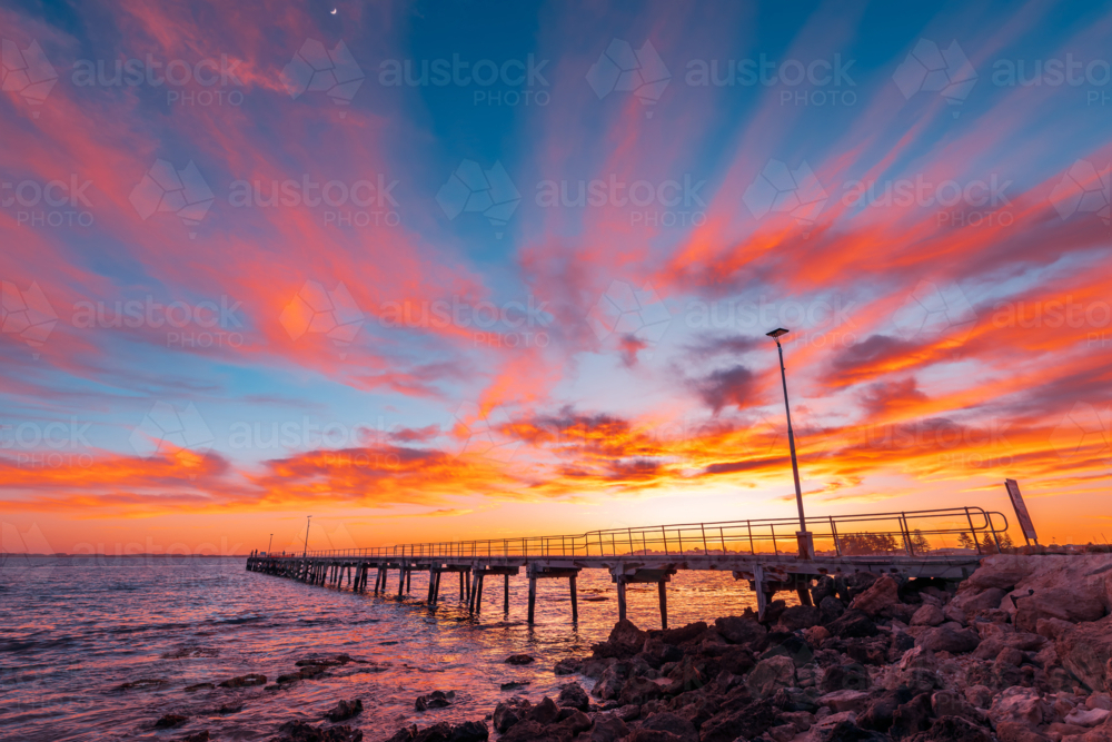 Robe jetty with fishermen during sunrise while viewed from the shore. - Australian Stock Image