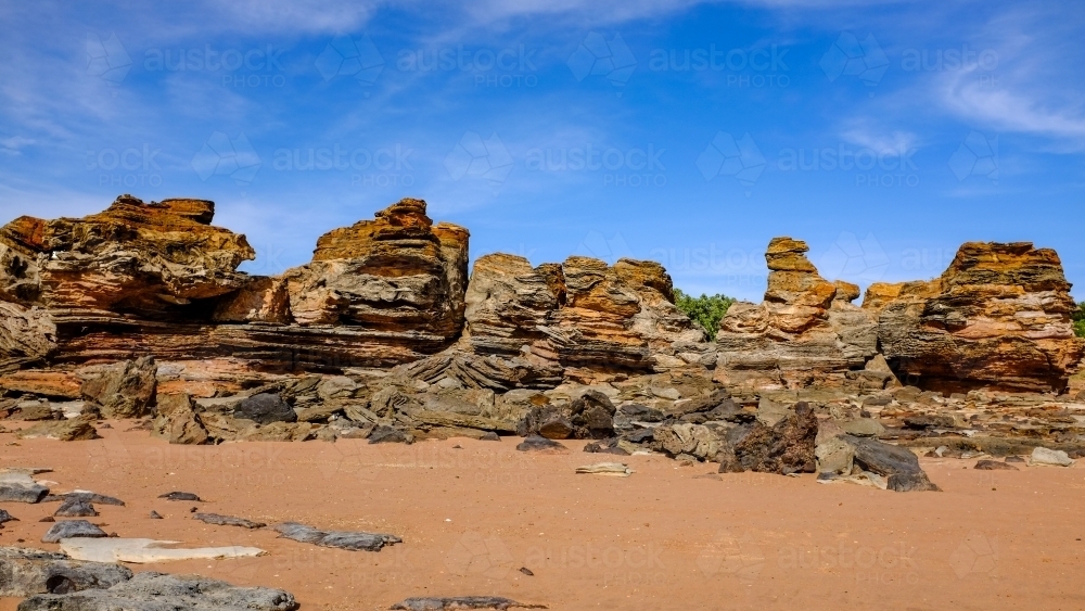 Rock formations on coastal beach beneath blue sky - Australian Stock Image