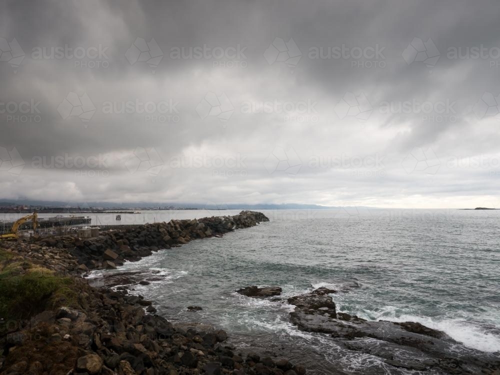 Rock groyne in the sea with a grey overcast sky - Australian Stock Image