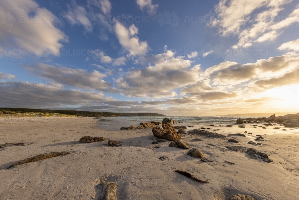 rock strewn shore of south coast beach with clouds in sky - Australian Stock Image