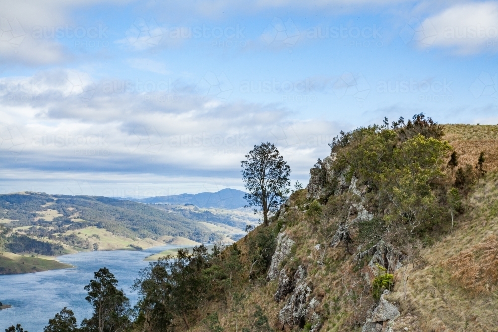 Rocky cliff and hilltop of mountain overlooking a dam - Australian Stock Image