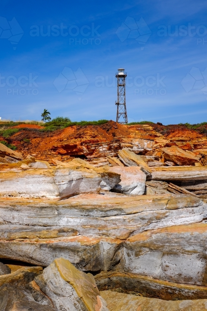 Rocky coastline with lighthouse tower against blue sky - Australian Stock Image