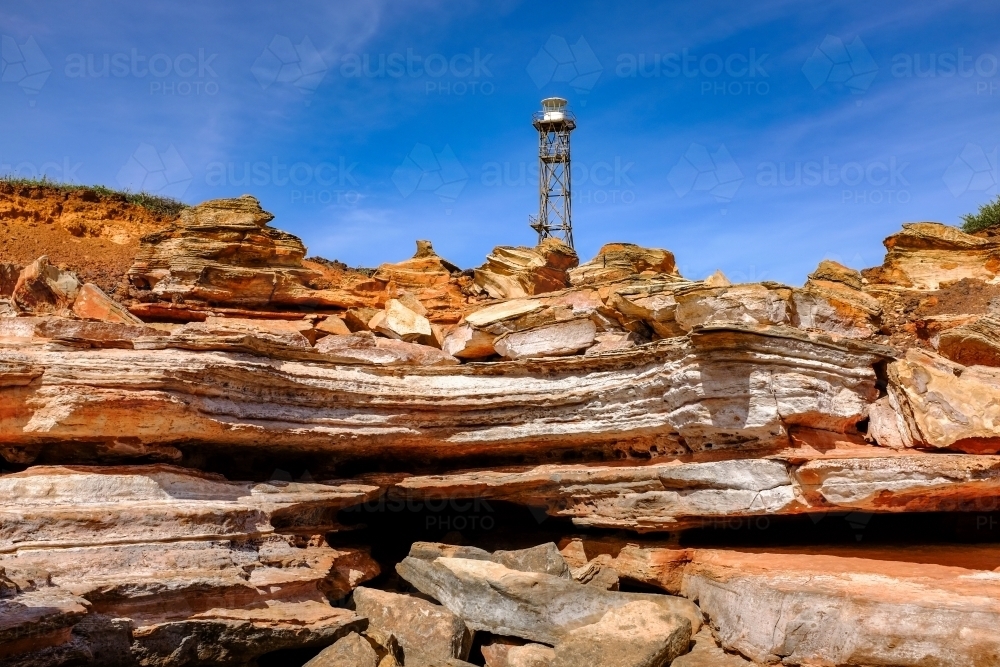 Rocky coastline with lighthouse tower against blue sky - Australian Stock Image
