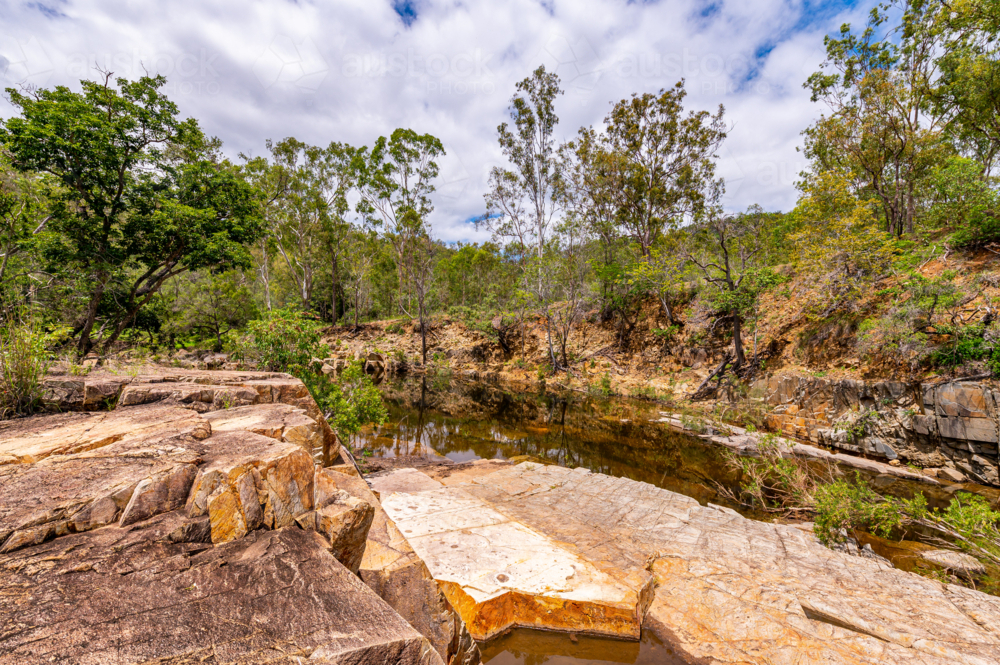 Rocky creek bed flowing through dense green bushland - Australian Stock Image