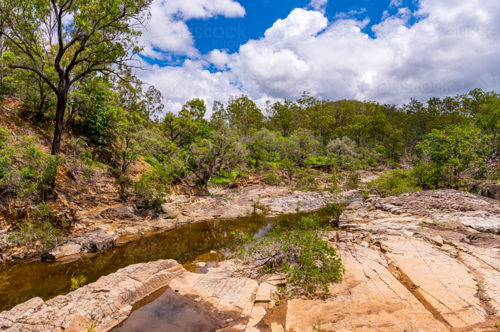 Rocky creek bed flowing through dense green bushland - Australian Stock Image