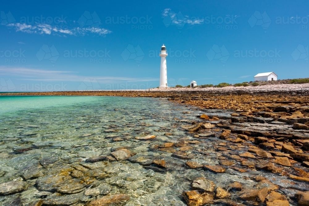 rocky shore with lighthouse and outbuildings under blue sky - Australian Stock Image