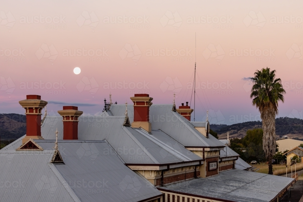 Rooftop of the historic Mudgee Railway Station with full moon in pink and purple twilight sky - Australian Stock Image