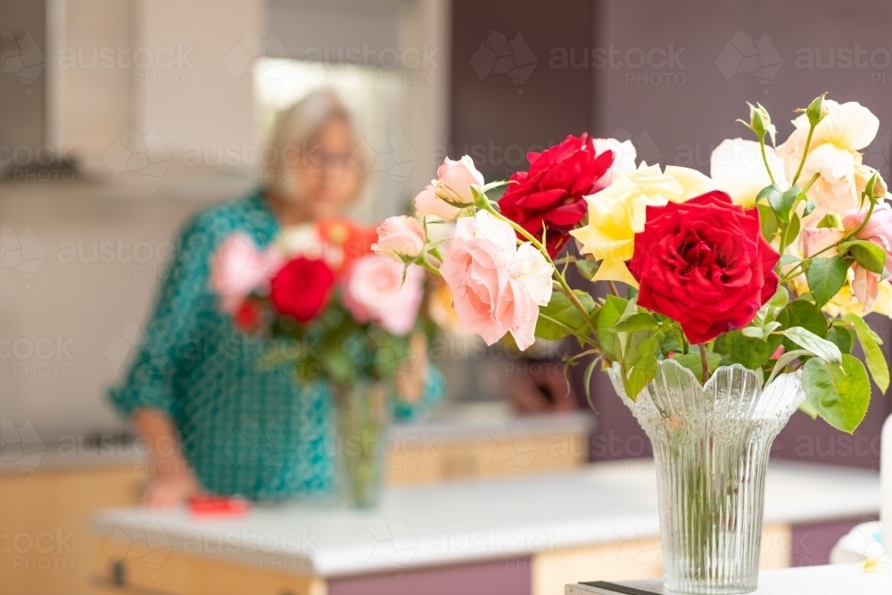 roses in vase with lady in background behind - Australian Stock Image