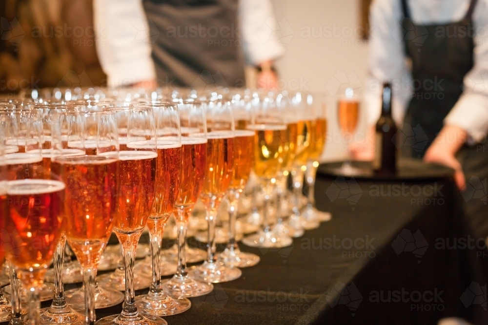 Row of glasses with sparkling wine and waiters in background - Australian Stock Image