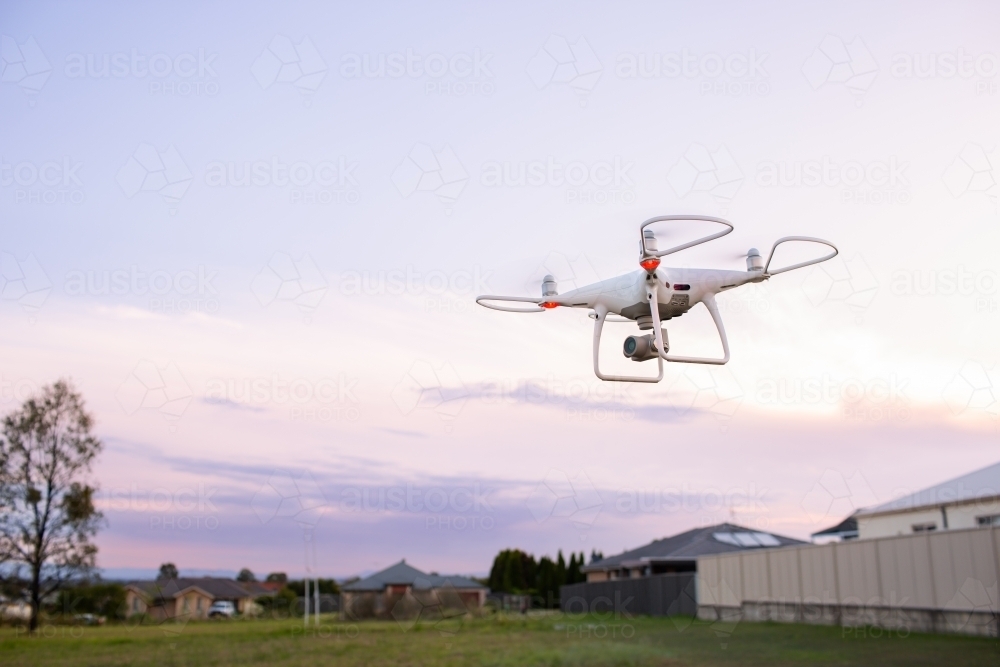 Image of RPA drone flying over edge of suburban area at dusk - Austockphoto