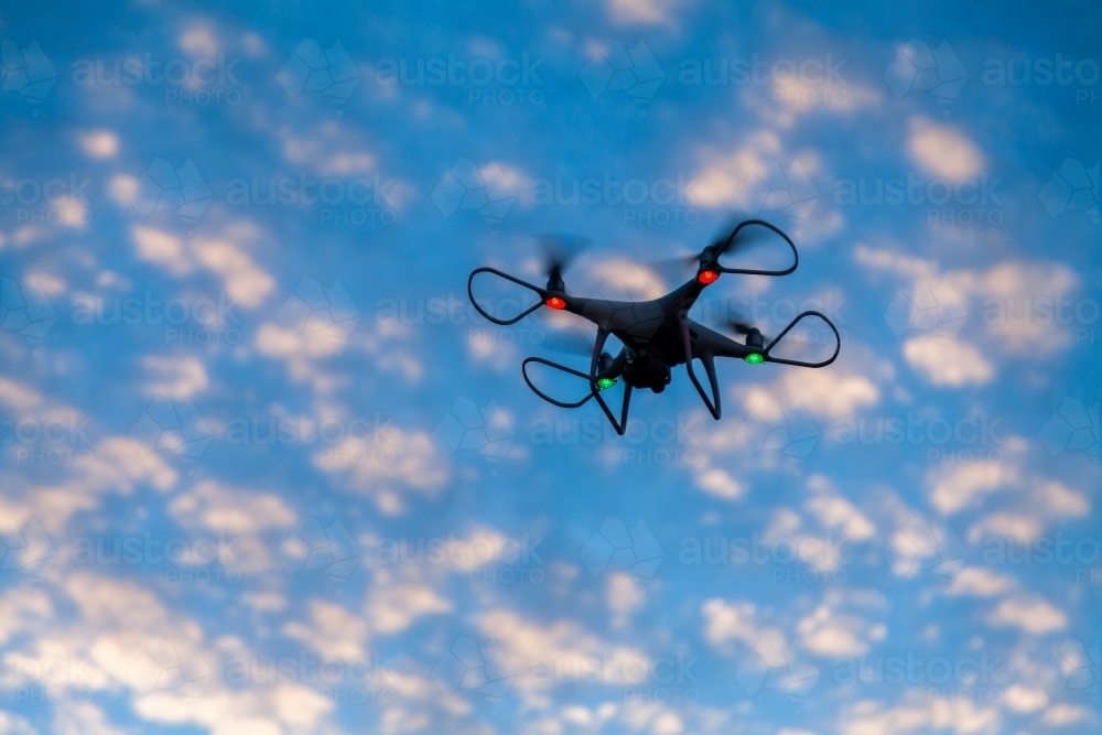 RPA drone hovering in clouded sky at dusk - Australian Stock Image