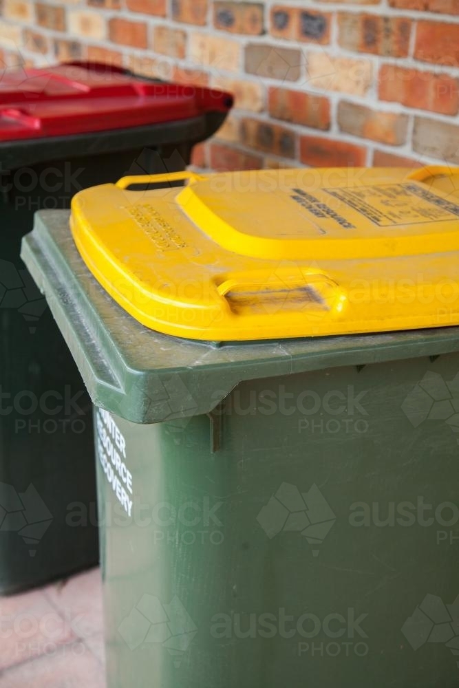 Rubbish and recycling bins beside the brick wall of a home - Australian Stock Image