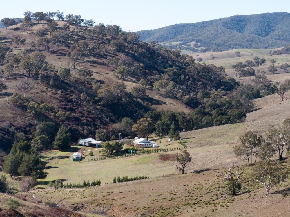 Rural homestead in a valley in hilly grazing farmland - Australian Stock Image