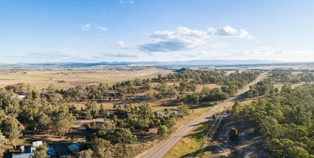 Rural road past paddocks and cliff to distant farmland - Australian Stock Image