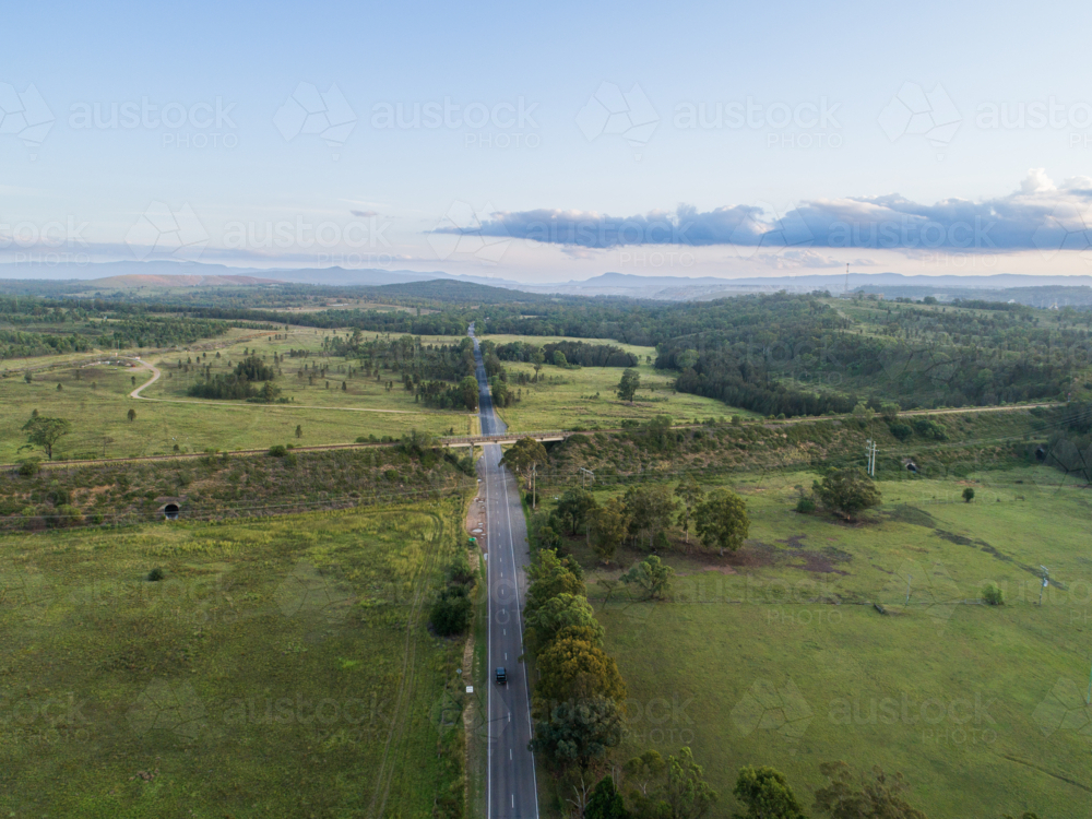 Rural road with train track overpass bridge from aerial view at dusk - Australian Stock Image
