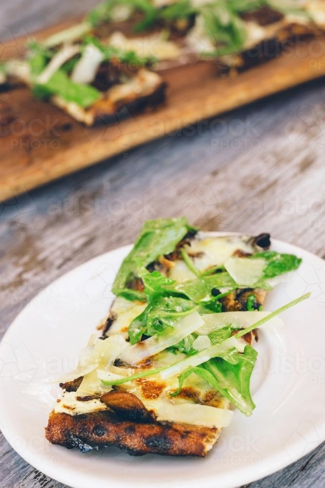 rustic pizza with rocket and parmesan on plate - Australian Stock Image