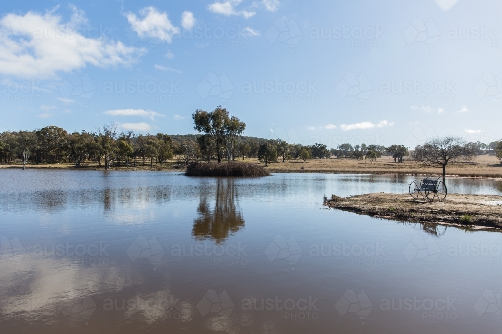 Rustic seat overlooking river water with trees on farm - Australian Stock Image