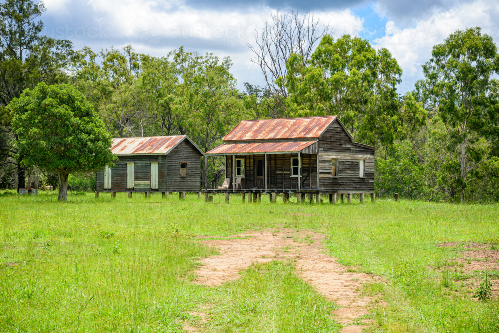 Rustic timber homesteads on wooden stumps with rusty corrugated iron roofs in rural landscape - Australian Stock Image
