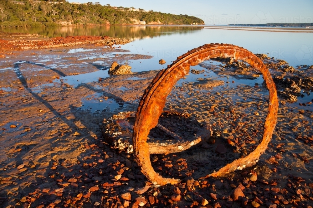 Rusting remains of an old boiler embedded in rock pools casting a long shadow - Australian Stock Image