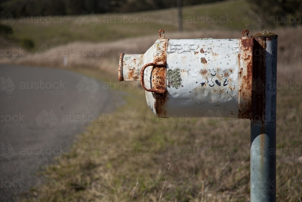 Rusty milk can mailbox beside rural road - Australian Stock Image
