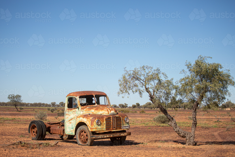 Rusty old truck cab and chassis beside a small tree - Australian Stock Image
