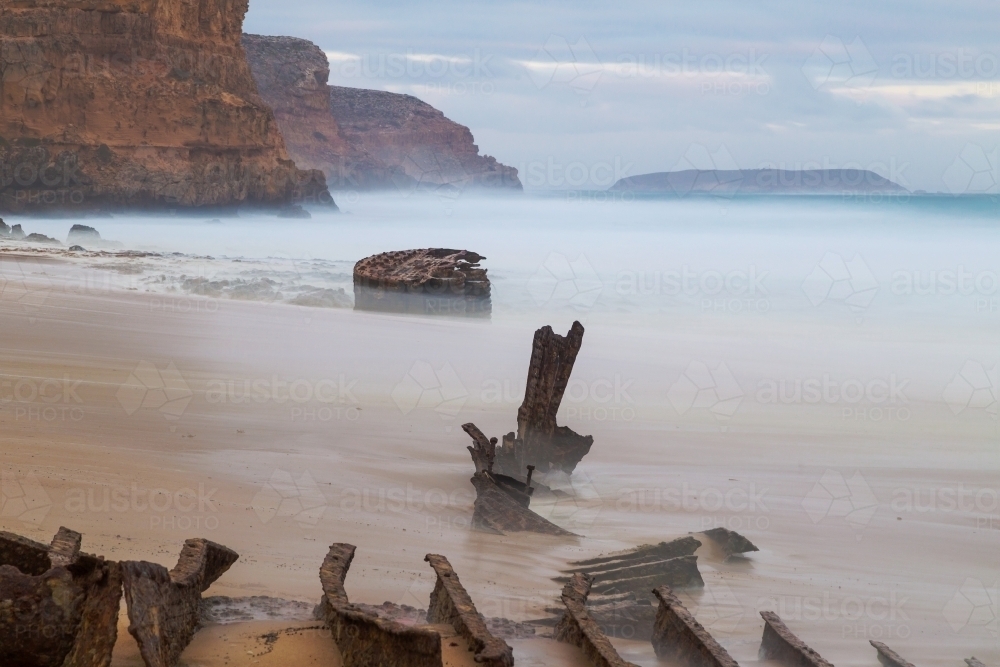 Rusty pieces of a shipwreck sticking out of the sand on an isolated beach - Australian Stock Image