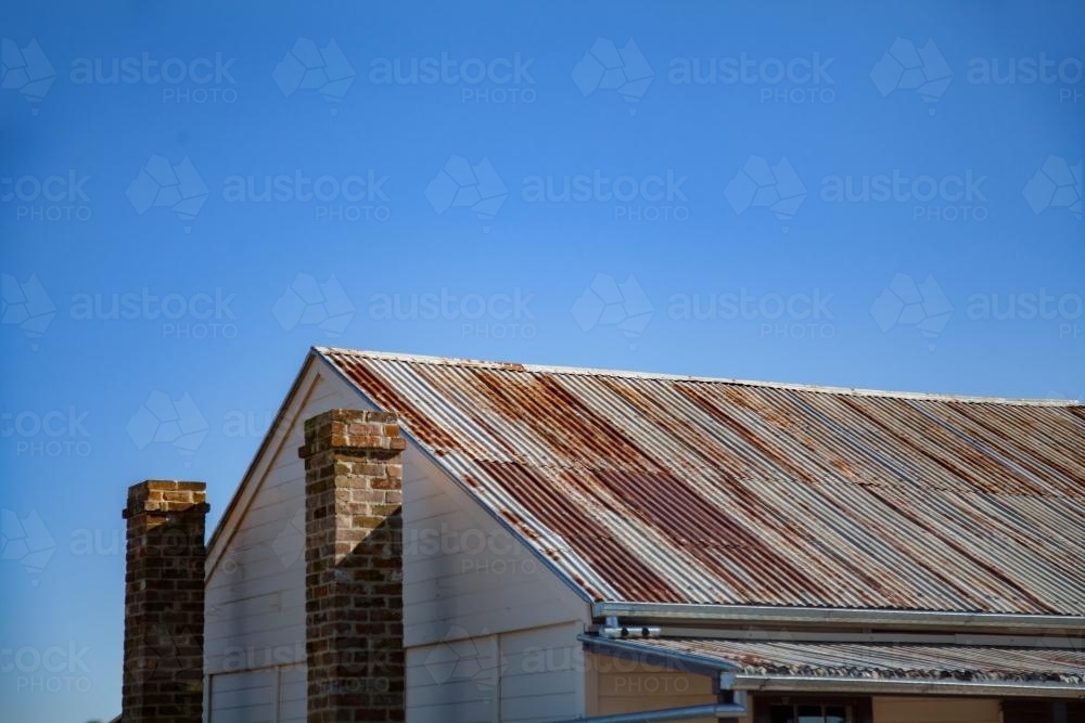Rusty roof and stone chimney of old building against blue sky - Australian Stock Image